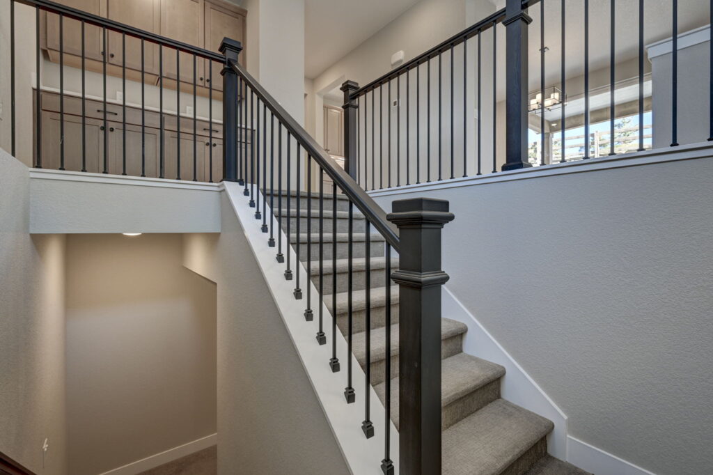 Carpeted staircase with dark wood handrail and metal balusters leading to an upper landing.