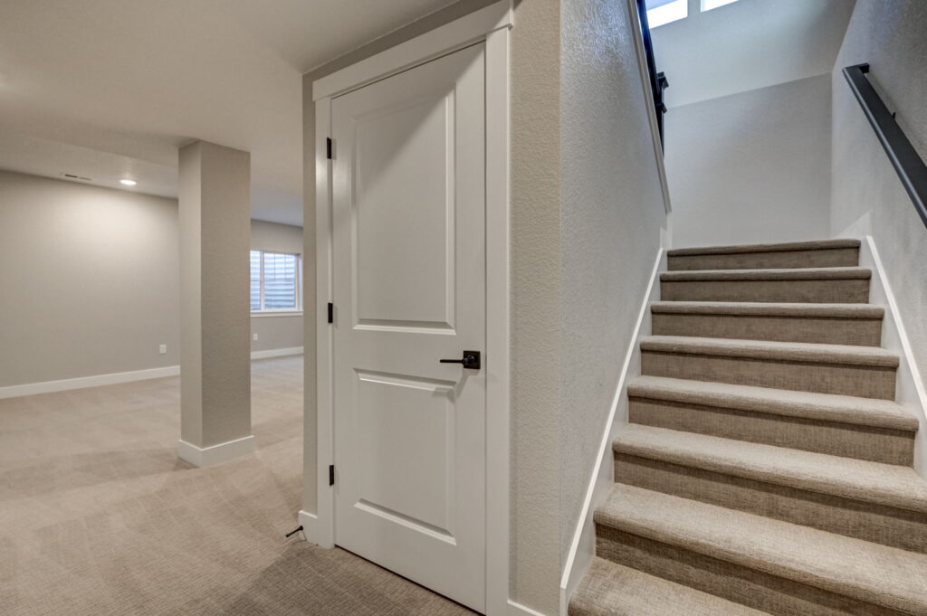 Lower-level space with carpeted stairs up to a landing and a closed white door under the stair.