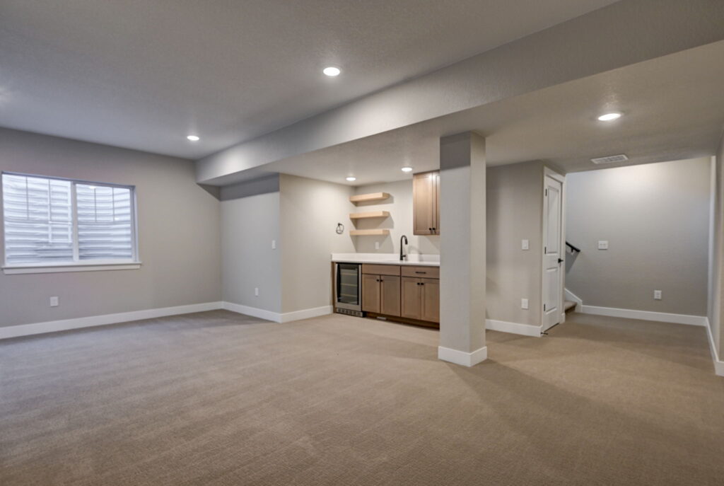 Spacious basement living area with wet bar, wine fridge, and staircase to upper level.