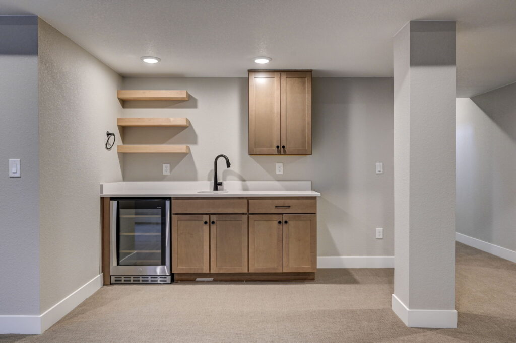 Close-up of a wet bar with wood cabinets, open shelves, sink, and small beverage refrigerator.