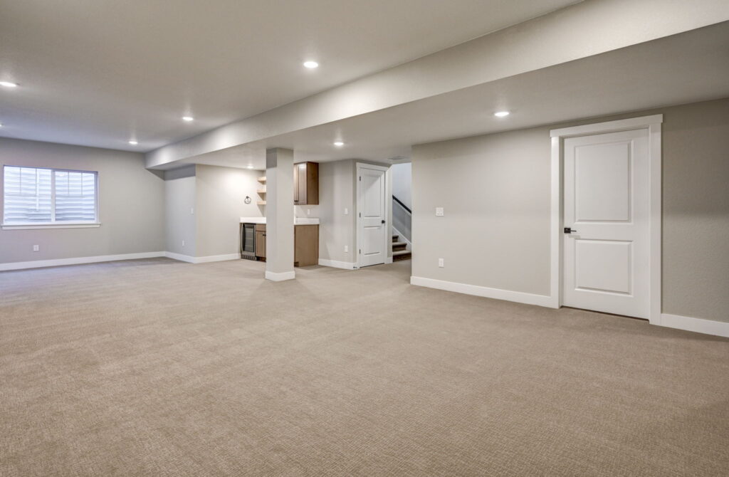 Open basement living area showing support column, small wet bar, stairs, and a window well.