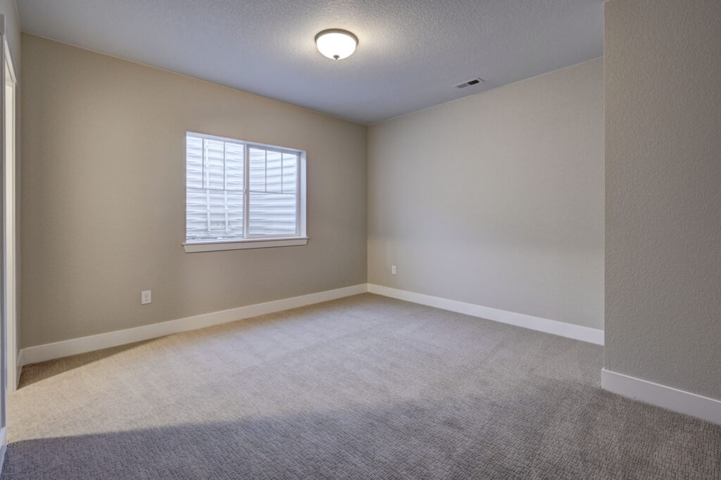 Empty carpeted room with a single window and soft overhead light.