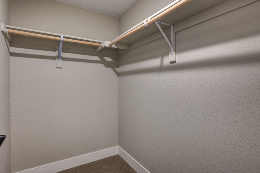 Empty walk-in closet with painted walls and a single wooden shelf-rod along two walls.