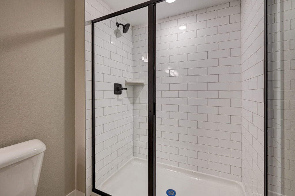 Glass shower enclosure with white subway tile and black metal frame and fixtures.