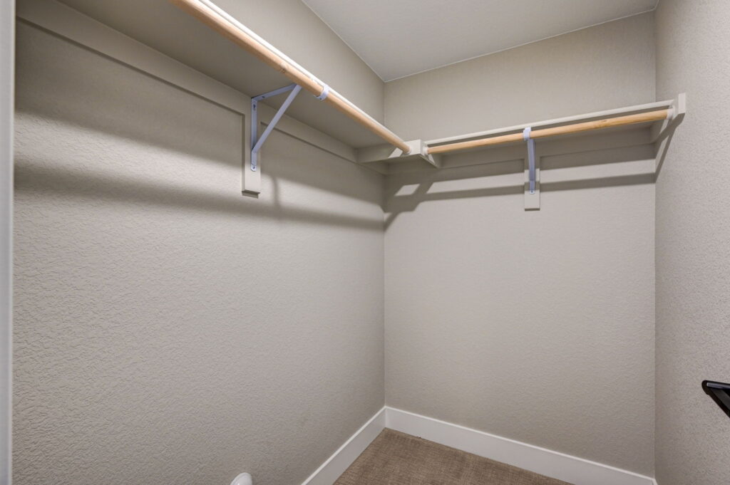 Small walk-in closet with two wood hanging rods and light-colored textured walls.