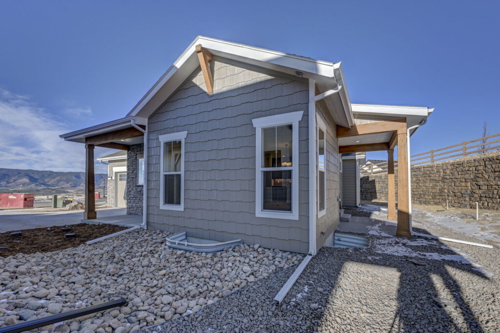 Exterior corner of a single-story home with gray shingle siding, white trim, and rock landscaping.