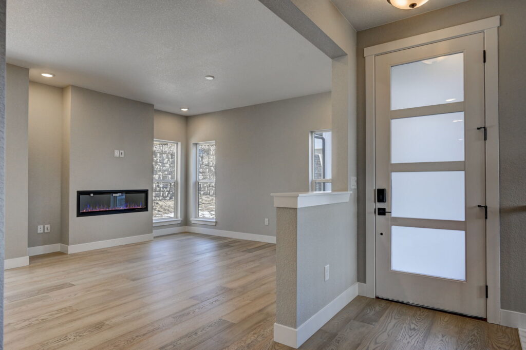 Entry area opening to a living room with wide-plank floors, corner windows, and a wall-mounted electric fireplace.