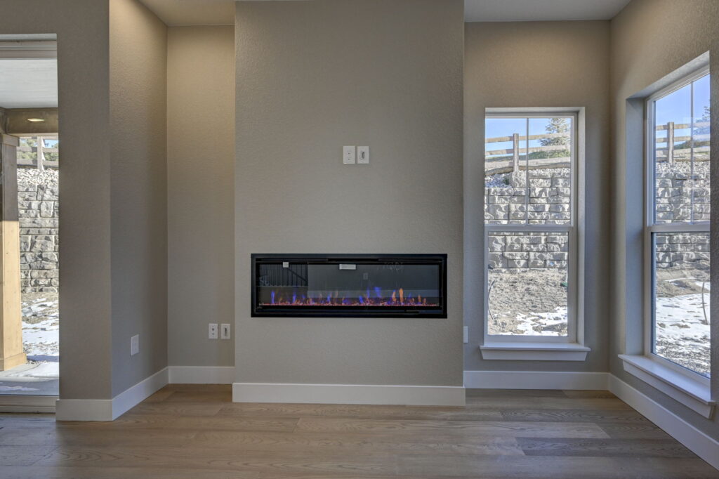 Wall-mounted rectangular electric fireplace centered between two tall windows with outdoor retaining wall visible.
