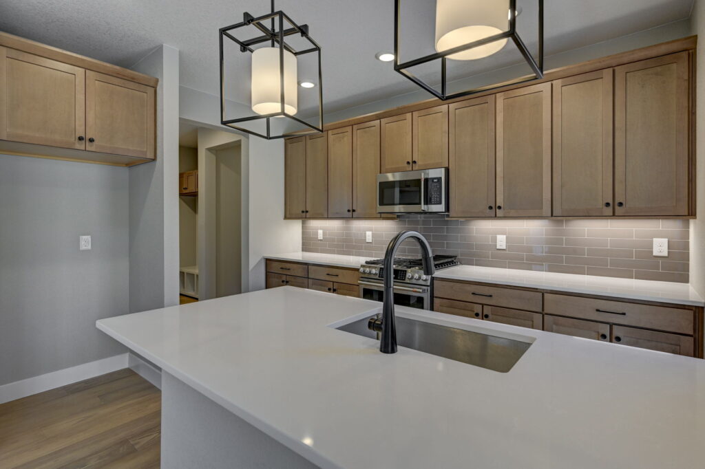 Close view of kitchen island countertop and faucet with pendant lighting and cabinetry behind.