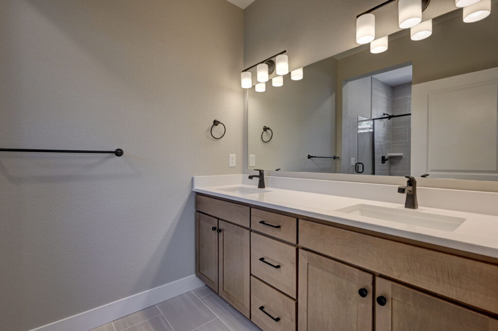 Bathroom vanity with double sinks, large mirror, wood cabinets, and modern light fixtures.