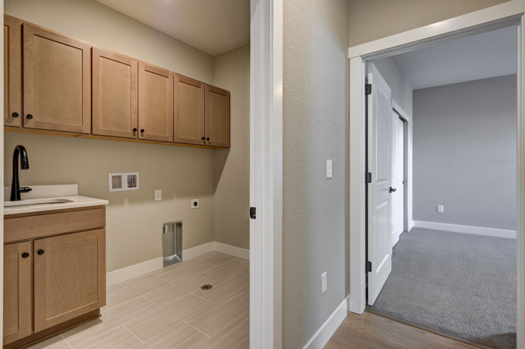 Laundry room with upper cabinets, utility hookups, and adjacent carpeted room entrance.