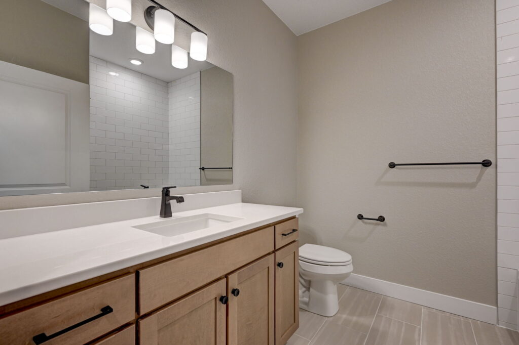 Bathroom vanity with light wood cabinets, white countertop, mirror, and toilet to the right.