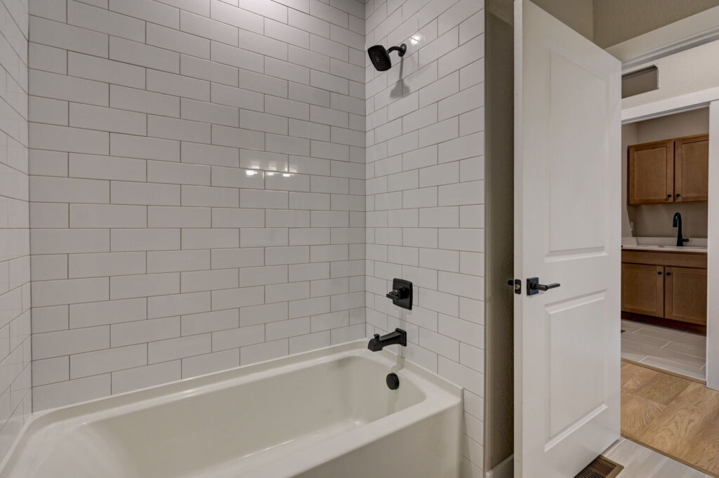 Bathtub and shower with white subway tile surround and dark fixtures, door open to hallway.