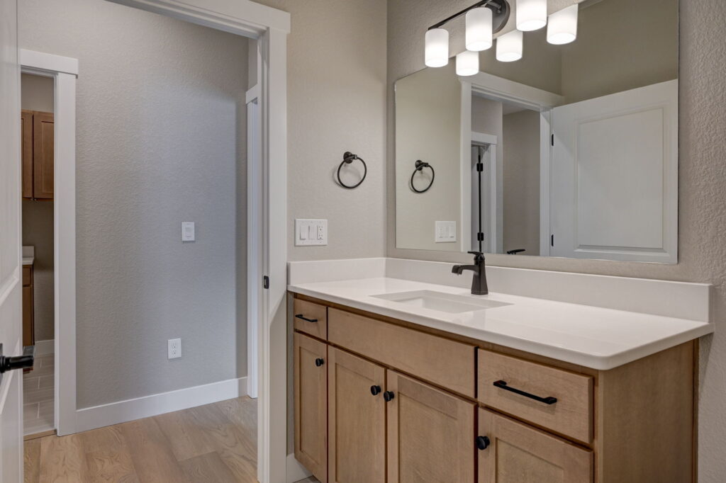 Single-sink bathroom vanity with mirror, light fixture, and wooden cabinets seen from an angle.