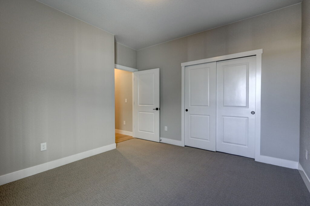 Empty carpeted bedroom with closed double-door closet and open entry door to a hallway.
