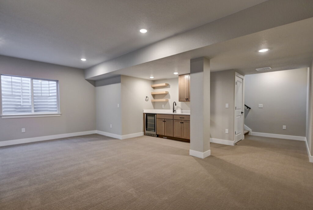 Finished basement room with built-in wet bar, beige carpet, recessed lighting and single window.