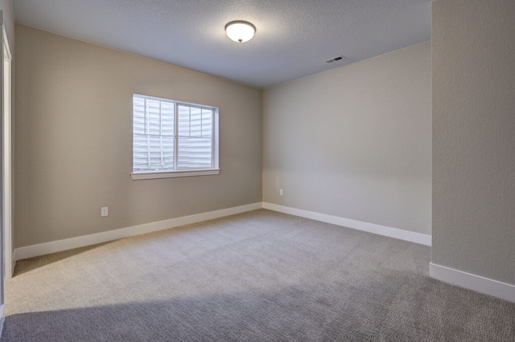 Empty carpeted room with a window and ceiling light, neutral walls and baseboards.