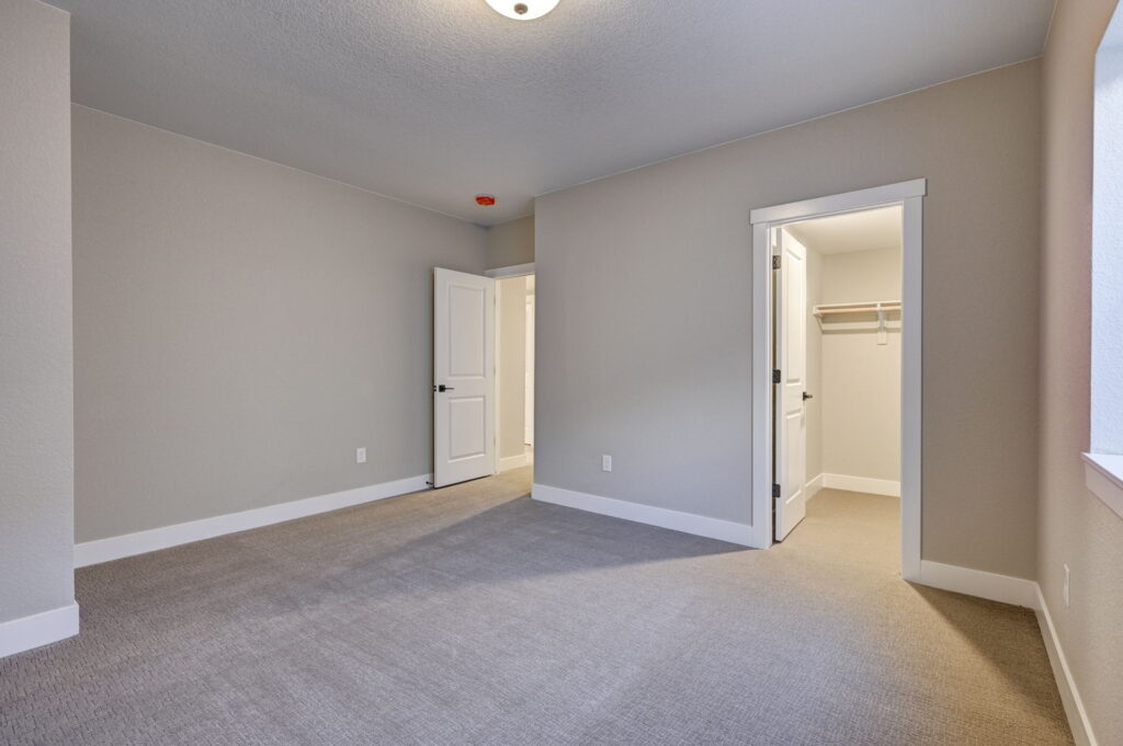 Carpeted bedroom with an open door to a small walk-in closet and neutral paint.