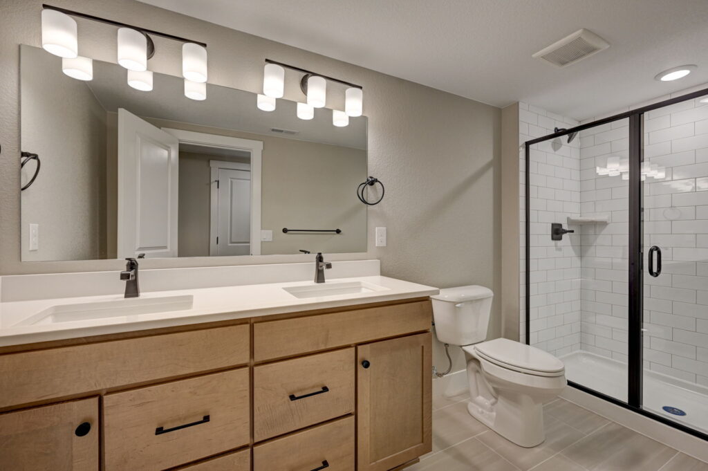 Bathroom vanity with double sinks, large mirror, wood cabinets and glass-enclosed shower visible at right.
