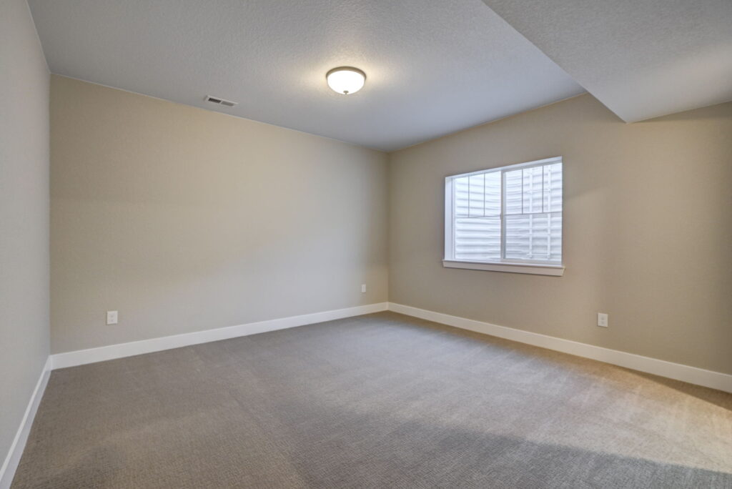 Empty carpeted room with beige walls, single window and ceiling light.