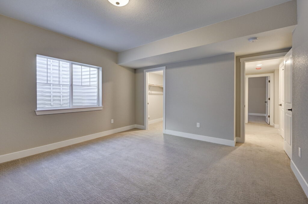 Spacious empty bedroom or living area with a window, closet doorway and hallway access.