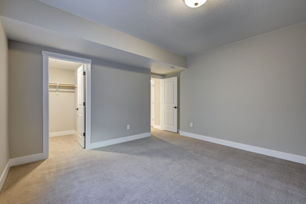 Empty carpeted room with two open doors and neutral gray walls under a ceiling light