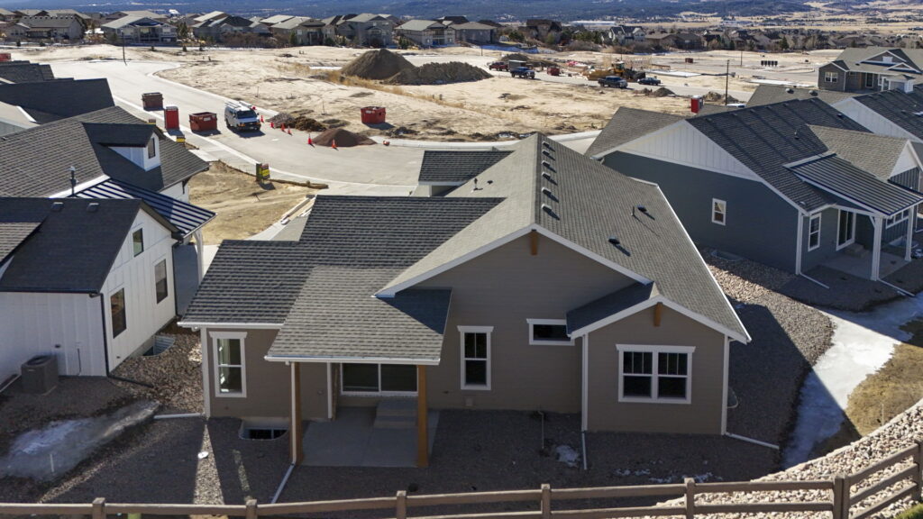 Aerial view of a single-story house on a sloped lot with gray roof and fenced yard.