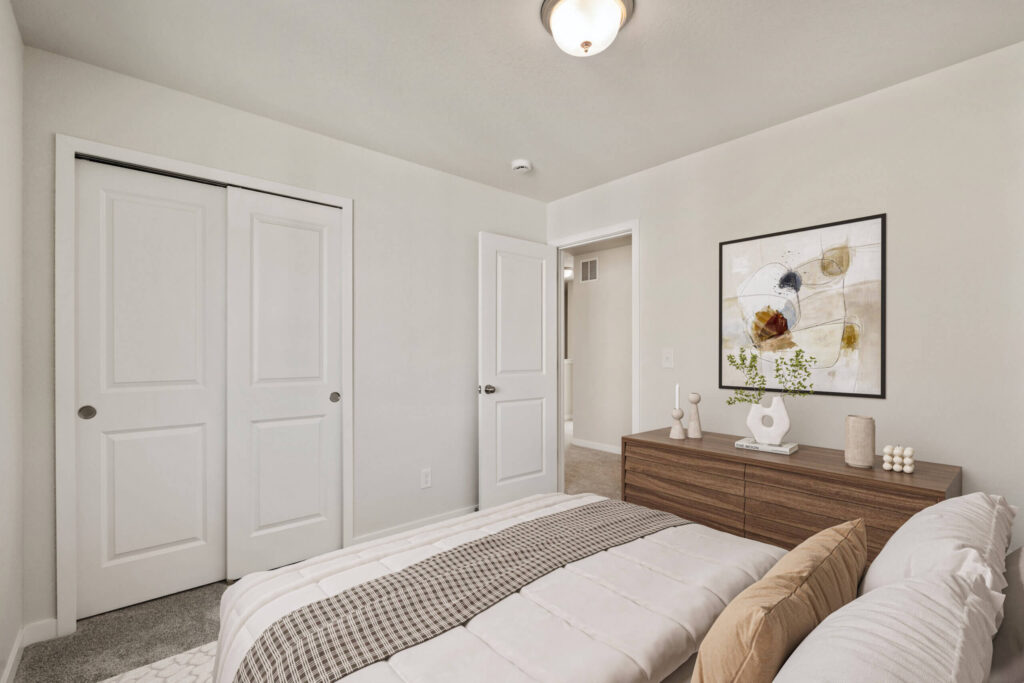 Neutral bedroom with bed, wooden dresser, framed abstract art, and closet with sliding doors.