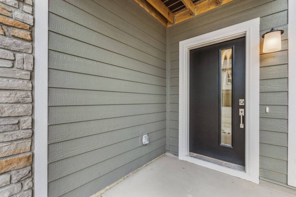 Entry alcove with dark modern front door, vertical sidelight, and exterior wall sconce.