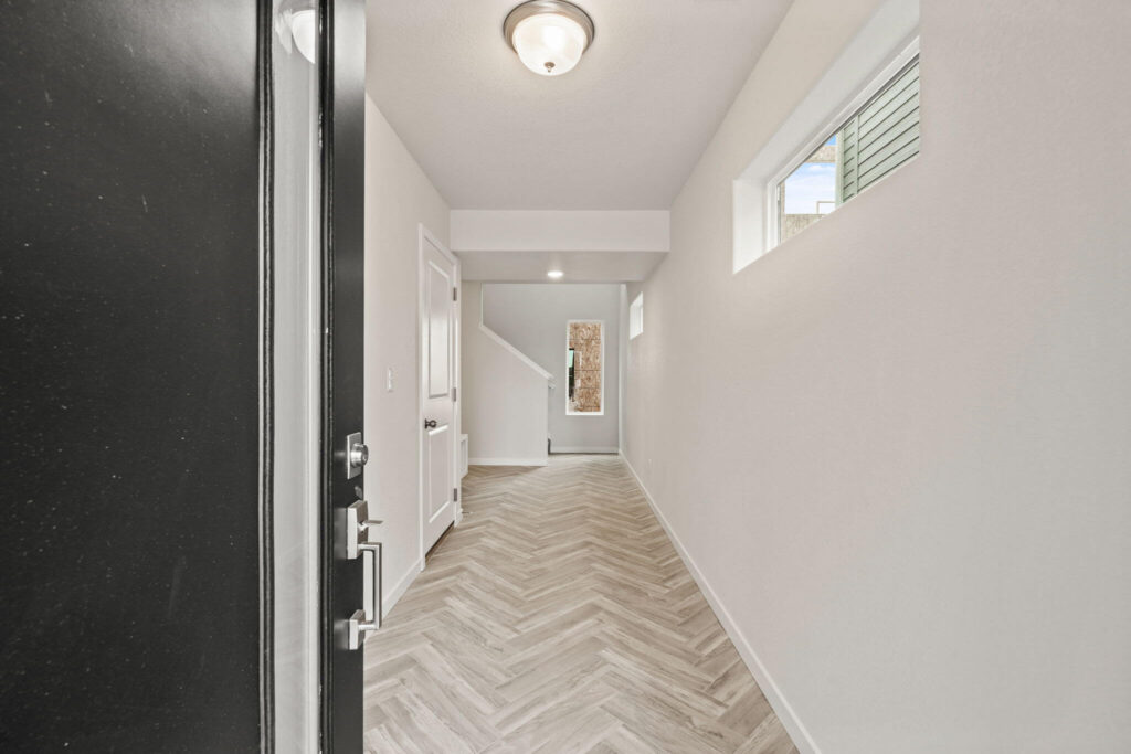 Long narrow entry hall with herringbone-pattern floor, small high window, and black door edge.