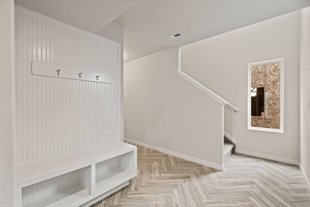 Mudroom-style bench with cubbies and coat hooks beside a stairway and a window looking outside.