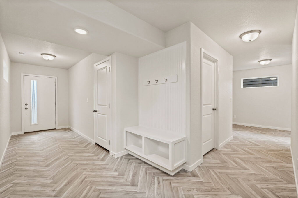 Open lower-level hallway with built-in bench, multiple doors, and herringbone-pattern flooring.