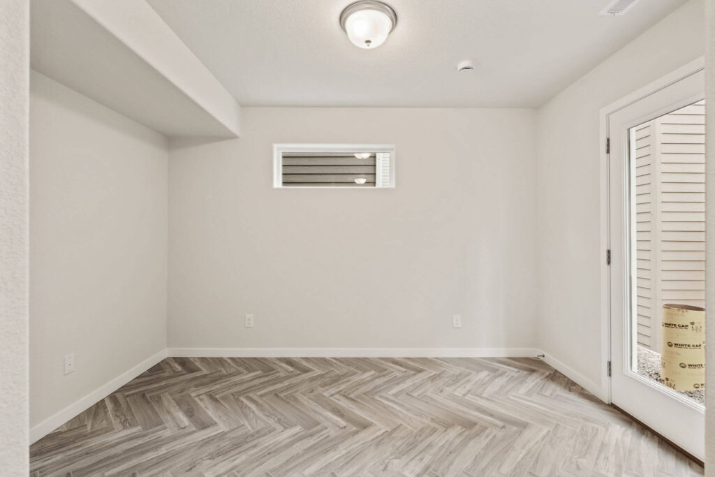 Empty room with herringbone-patterned light wood floor and small horizontal window near ceiling.