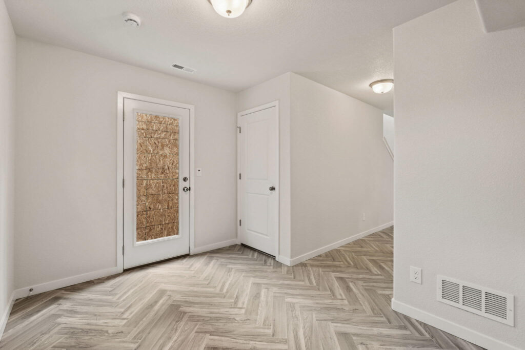 Interior view of a room with a door to exterior and a closed interior door, herringbone floor.
