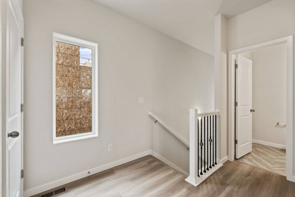 Small upstairs landing with narrow vertical window, wood-look floor, and stair railing with iron balusters.