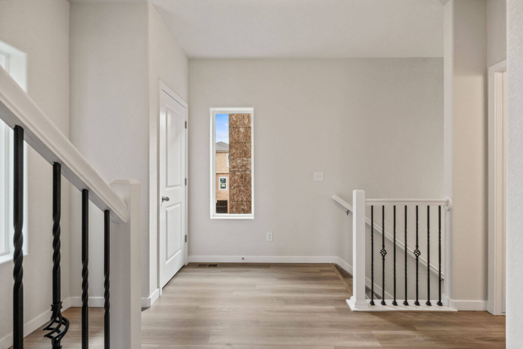 Bright upstairs landing area with narrow window, stair rail with iron balusters, and a closed closet door.