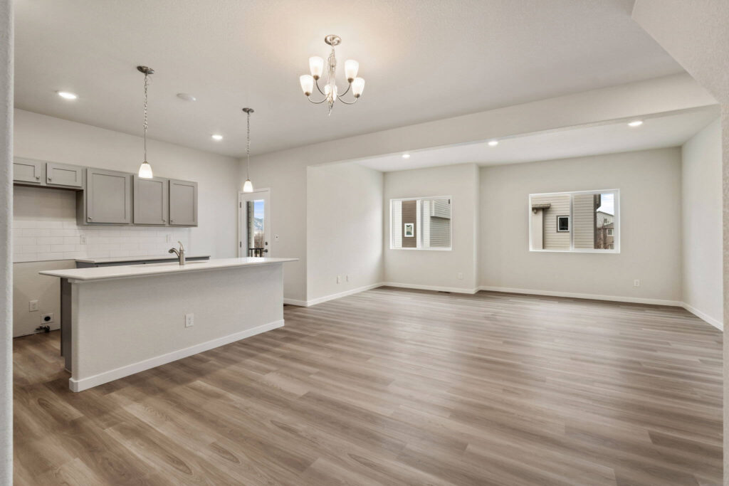 Open-plan living area with kitchen island, light wood-look floors and pendant lights.