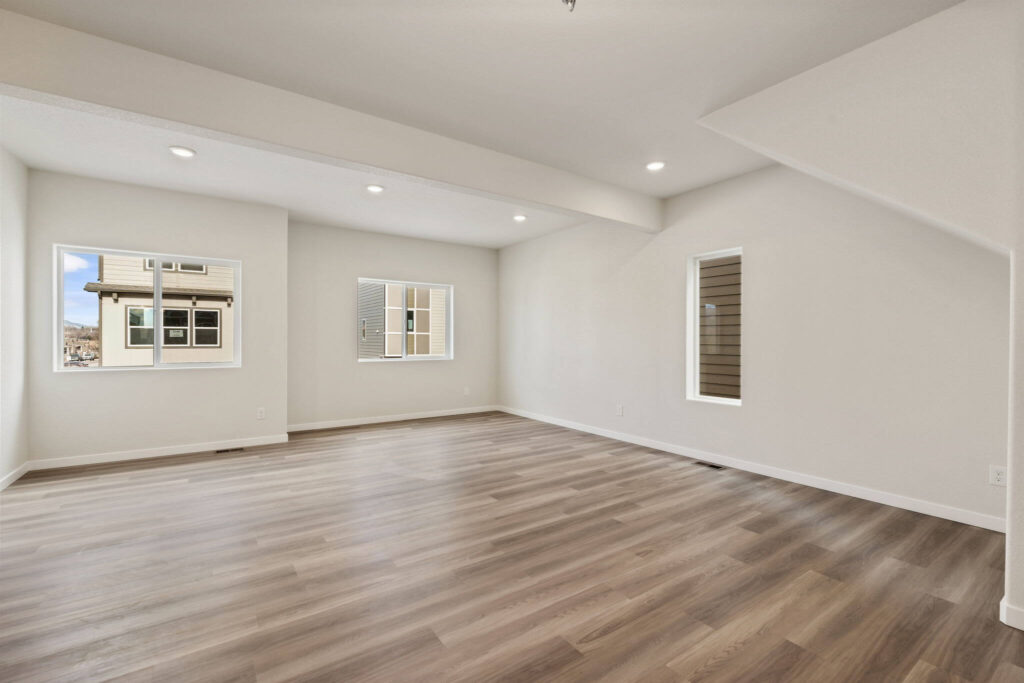 Spacious living room with exposed ceiling beam, three windows and wood-look floors.