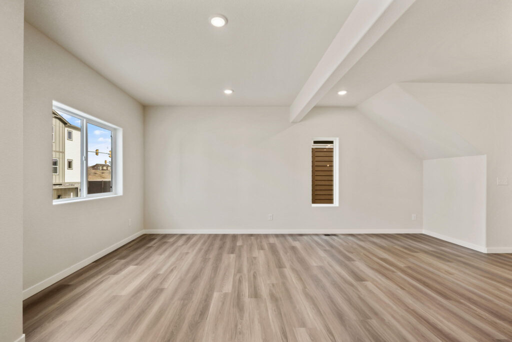 Empty room with sloped ceiling section, narrow vertical window and wide horizontal window.