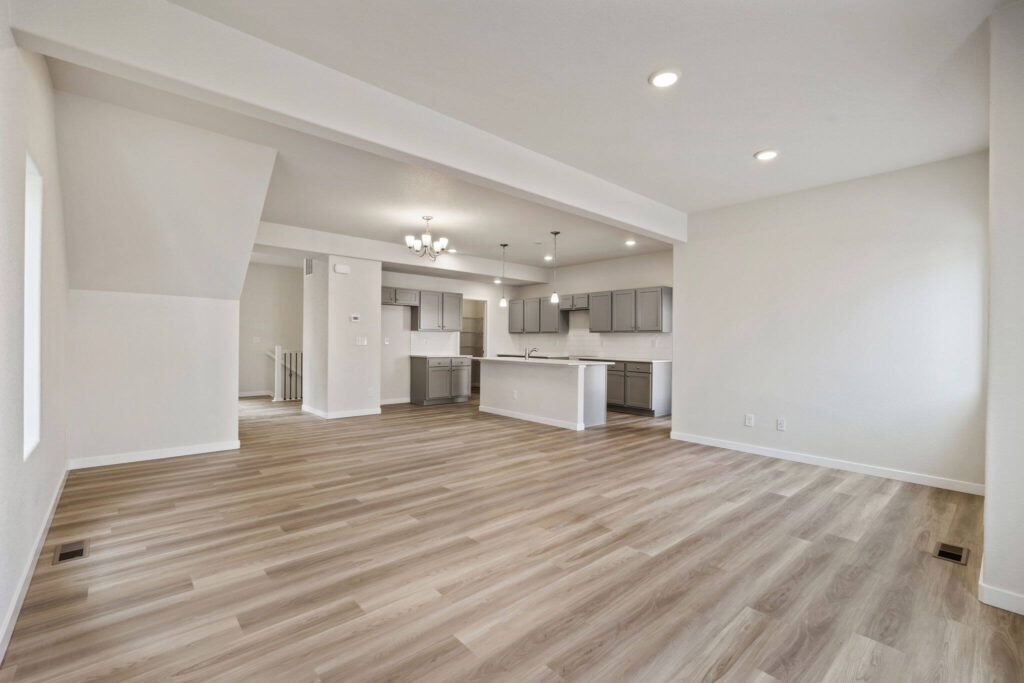 Open living area with light wood-look flooring and white walls opening to a kitchen with island.