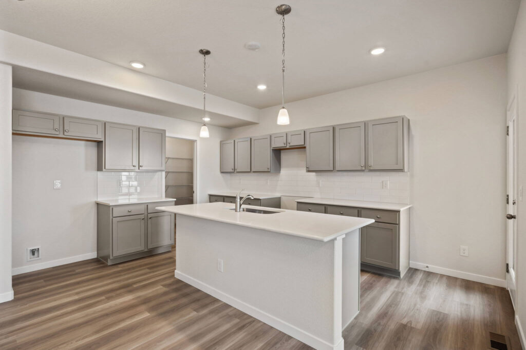 Kitchen seen from an angle showing island, gray upper cabinets, and light wood-look flooring.
