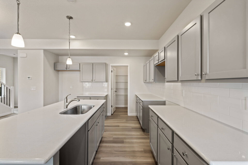 Long galley-style kitchen view with island sink, gray cabinets and pantry door at far end.