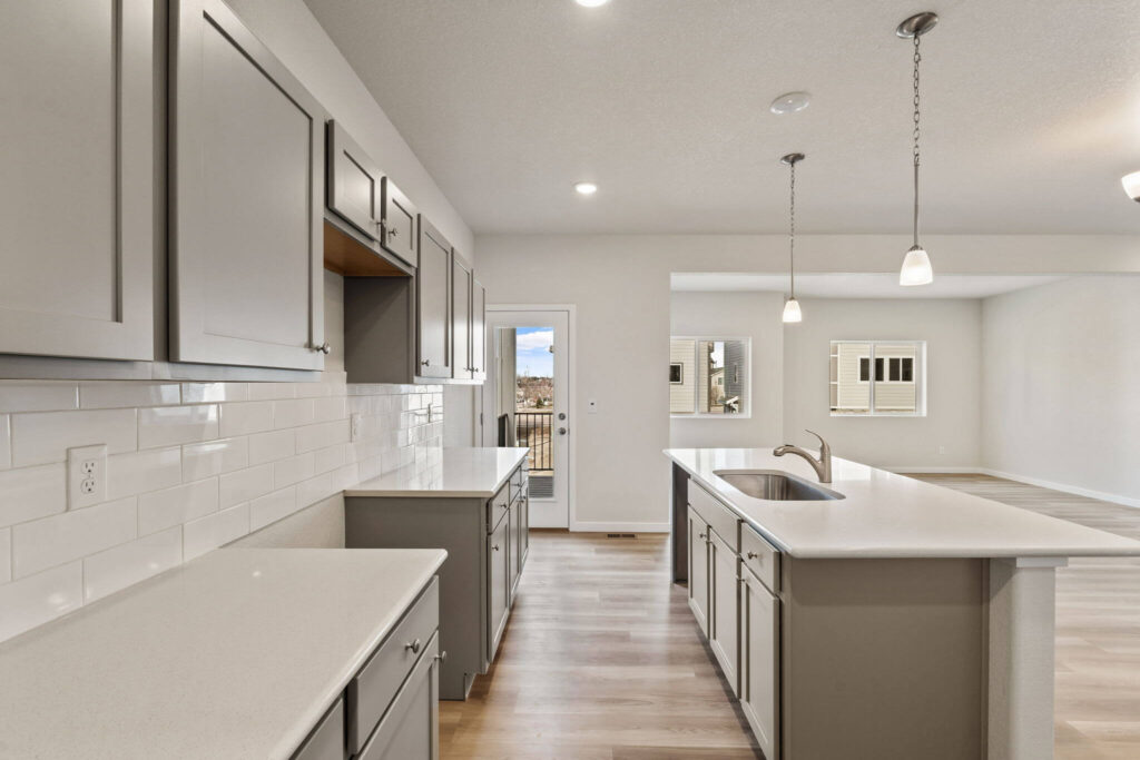 Bright kitchen with long island, gray cabinets, and subway tile backsplash.