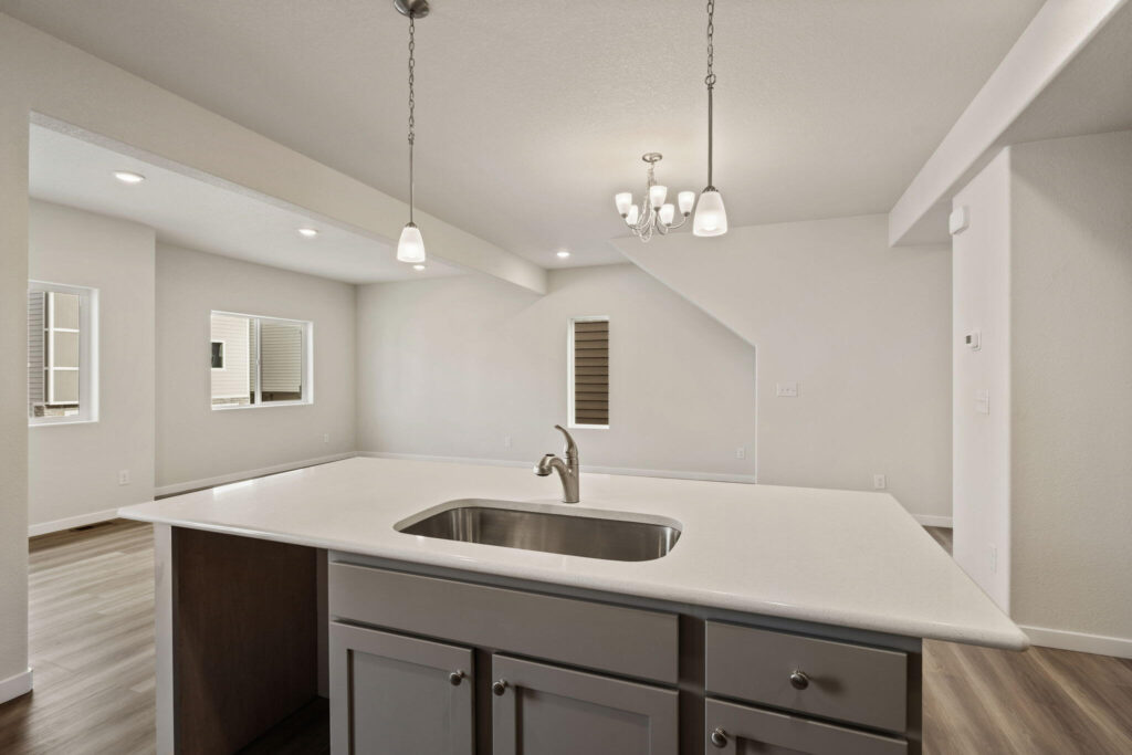 Island countertop with sink looking toward an open living area and chandelier.