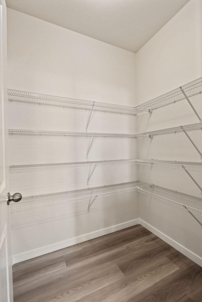 Walk-in pantry with multiple white wire shelving units and wood-look floor.