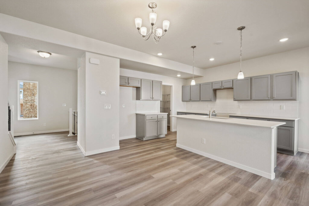 Wide view of an open kitchen with a long island, upper cabinets, and chandelier lighting.