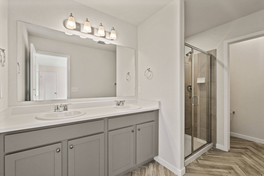 Bathroom vanity with double sinks, large mirror, and a tiled glass shower stall to the right.
