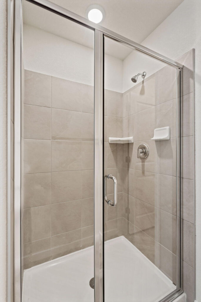 Glass-enclosed tiled shower with chrome hardware and built-in soap ledges.