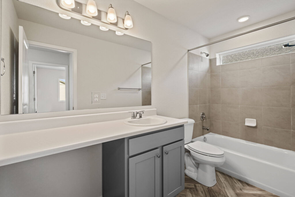 Bathroom with single sink vanity, large mirror, tub-shower with tiled surround, and overhead vanity lights.