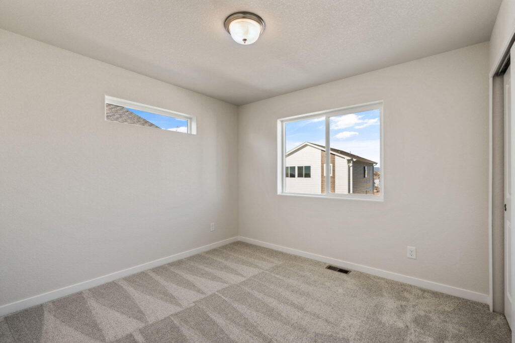 Corner bedroom with two windows including a narrow high window, carpeted floor, and a ceiling light.